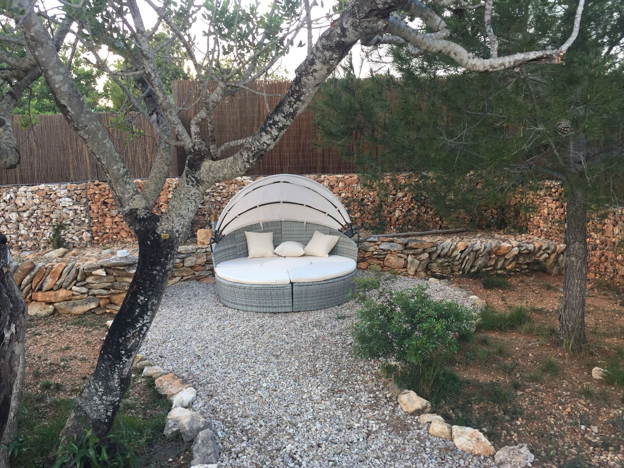 A circular outdoor seating area with a canopy, surrounded by stone walls and trees.