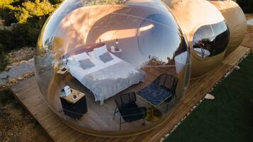 A transparent dome structure with a bed, a table, and two chairs inside.