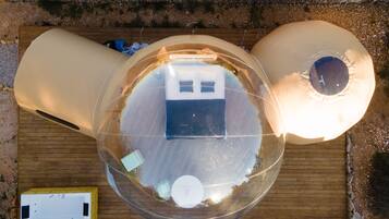 Una habitación esférica transparente con una cama, una mesita y una silla.