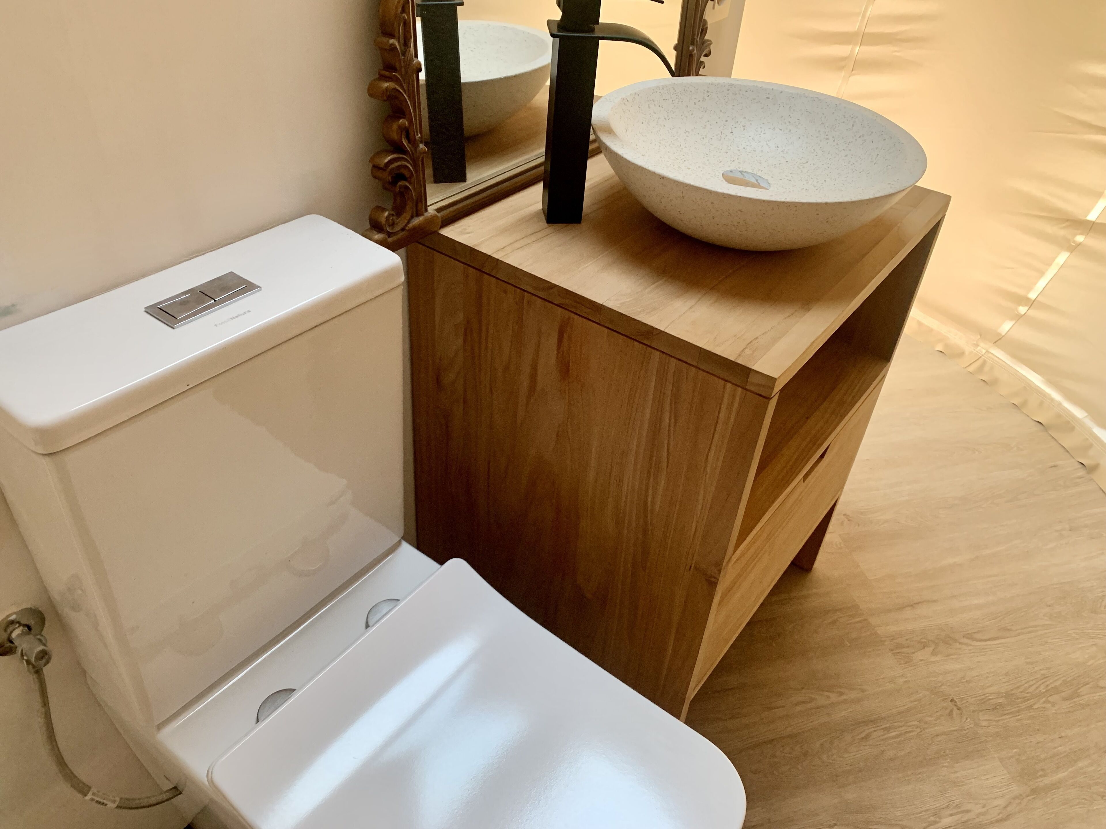 A bathroom with a white toilet, a wooden vanity with a large bowl sink, and a mirror above the sink.