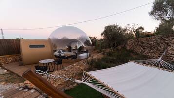 A transparent dome structure with a seating area inside, surrounded by a stone wall and greenery.