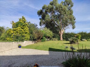 Un jardín ajardinado con diversos árboles, un camino de grava y un banco.