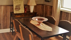 A dining area with a wooden table, chairs, a lamp, a mirror, and a wall-mounted sign. - The Red 6 at Grand Forks (Grand Forks)