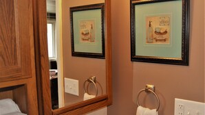 A bathroom with a wooden cabinet, a mirror, a framed picture, a towel ring, and a soap dispenser. - The Red 6 at Grand Forks (Grand Forks)
