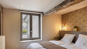 Ein Schlafzimmer mit großem Fenster, einem Bett mit weißer Bettwäsche, einem Holz-Kopfschild und einer Wand mit ornamentalem Wandpapier.