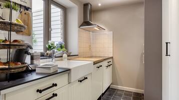 Une cuisine moderne avec des meubles blancs, un plan de travail noir, une hotte en acier inoxydable et une fenêtre équipée de stores.