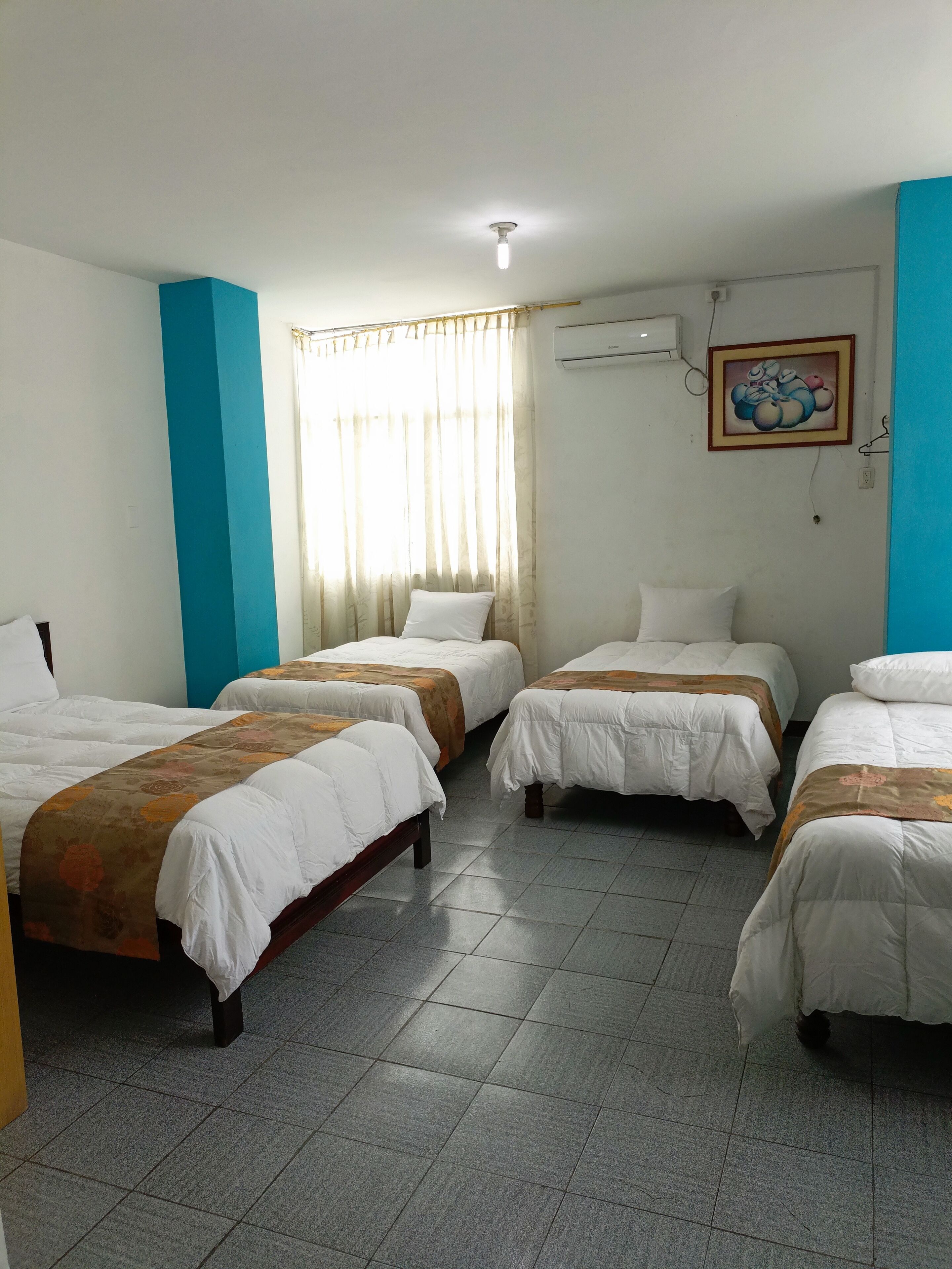 A hotel room with four single beds, a tiled floor, a window with curtains, an air conditioning unit, and a framed picture on the wall.