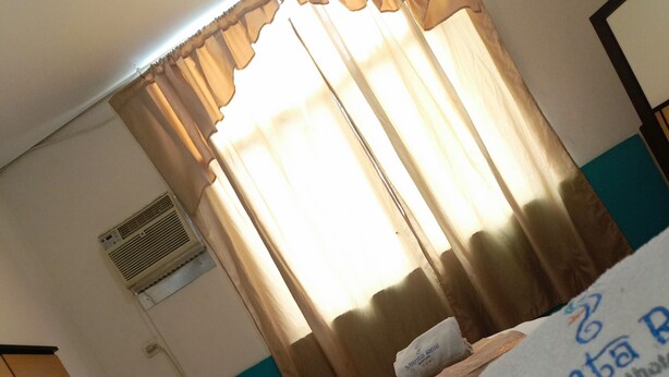 Habitación de hotel con dos camas, ventana con cortinas, equipo de aire acondicionado y almohada con el nombre del hotel.