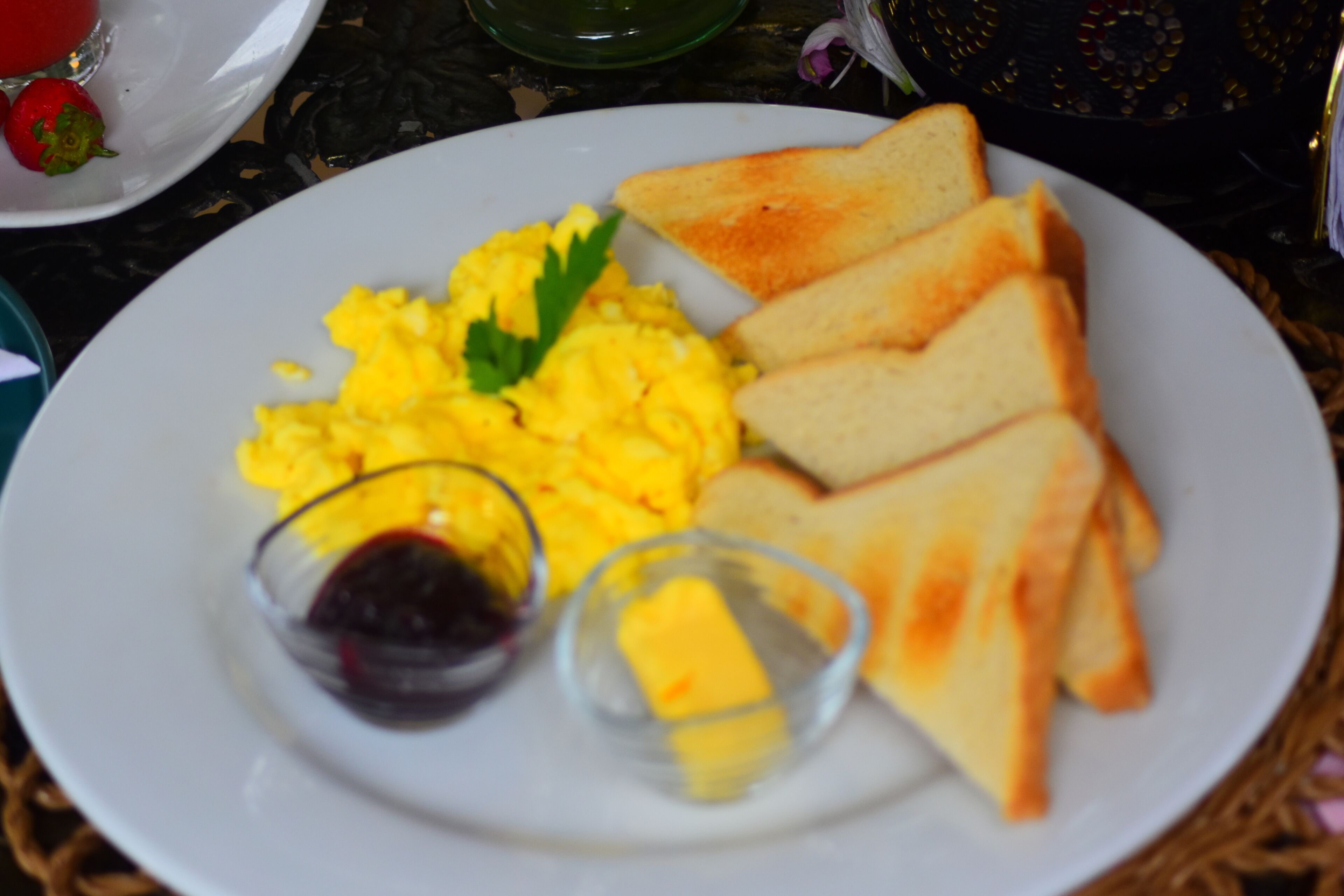 A plate with scrambled eggs, toast, butter, and jam.