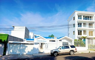 A modern hotel with a gated entrance, a parked SUV, and a clear blue sky.