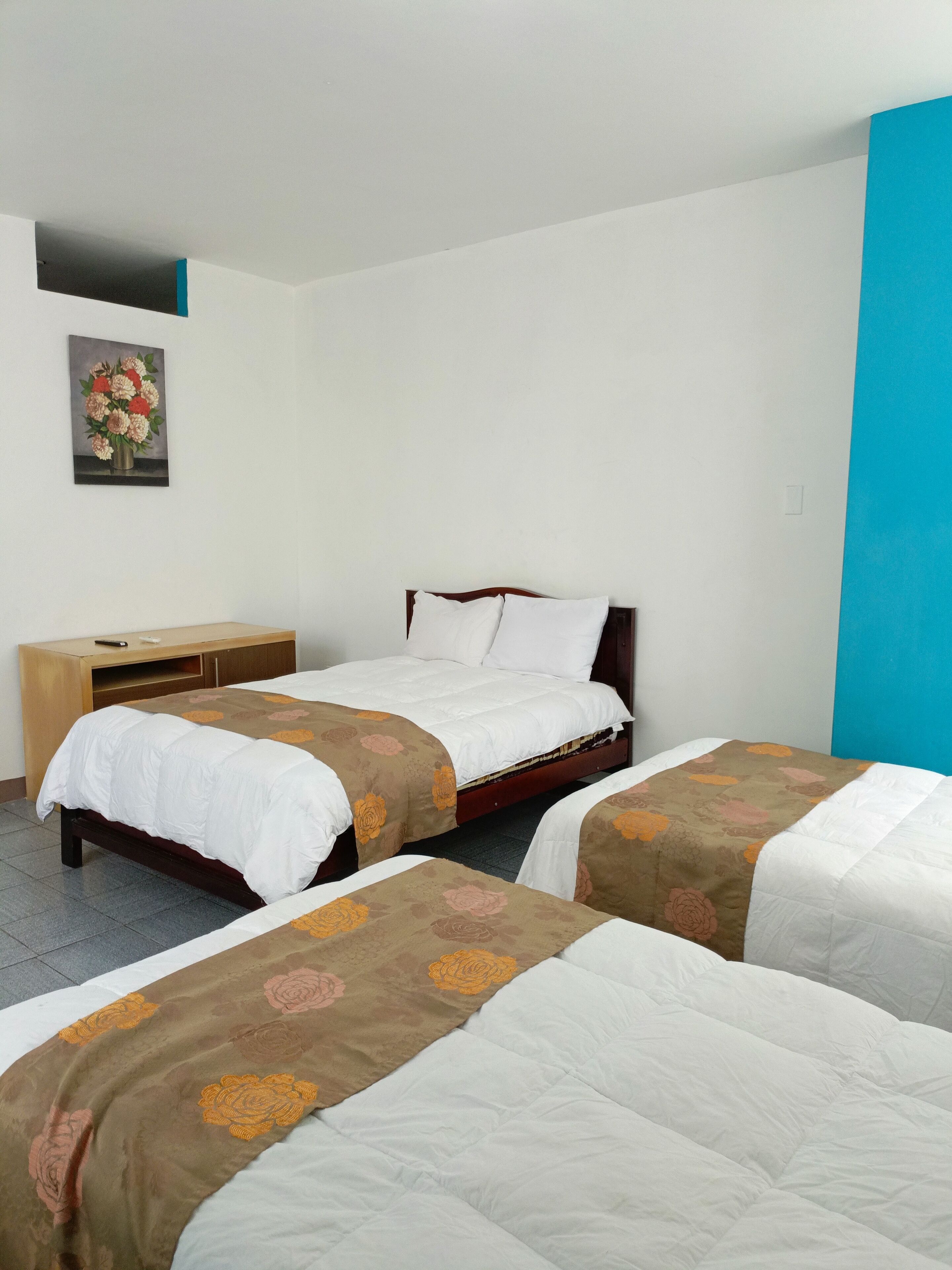 Una habitación de hotel con dos camas individuales, una mesita de noche de madera, una pequeña mesa y un cuadro en la pared.