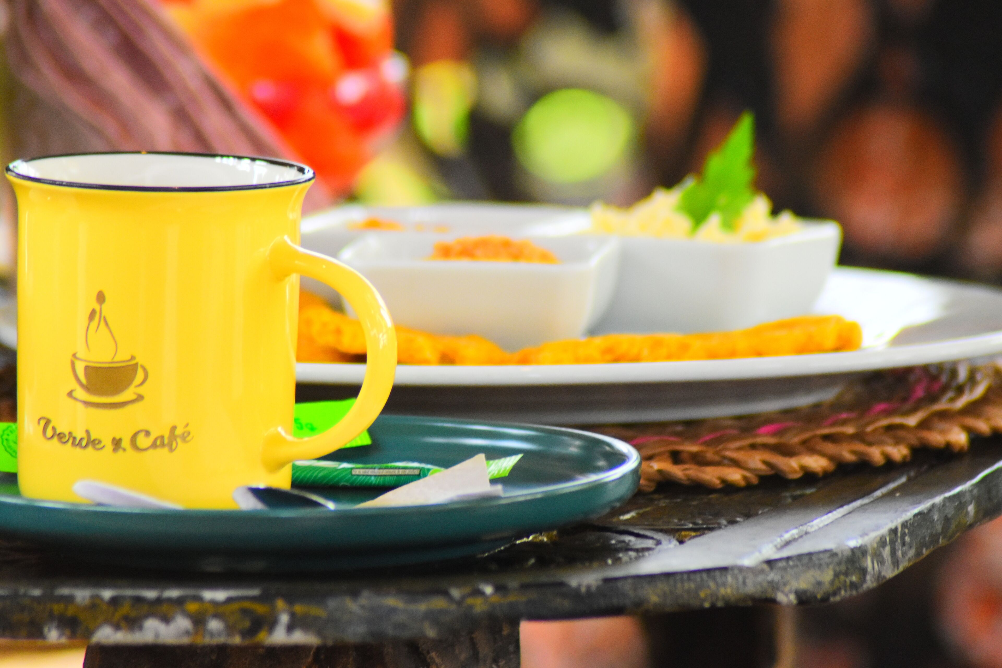 A yellow mug with a café logo on a green saucer.
