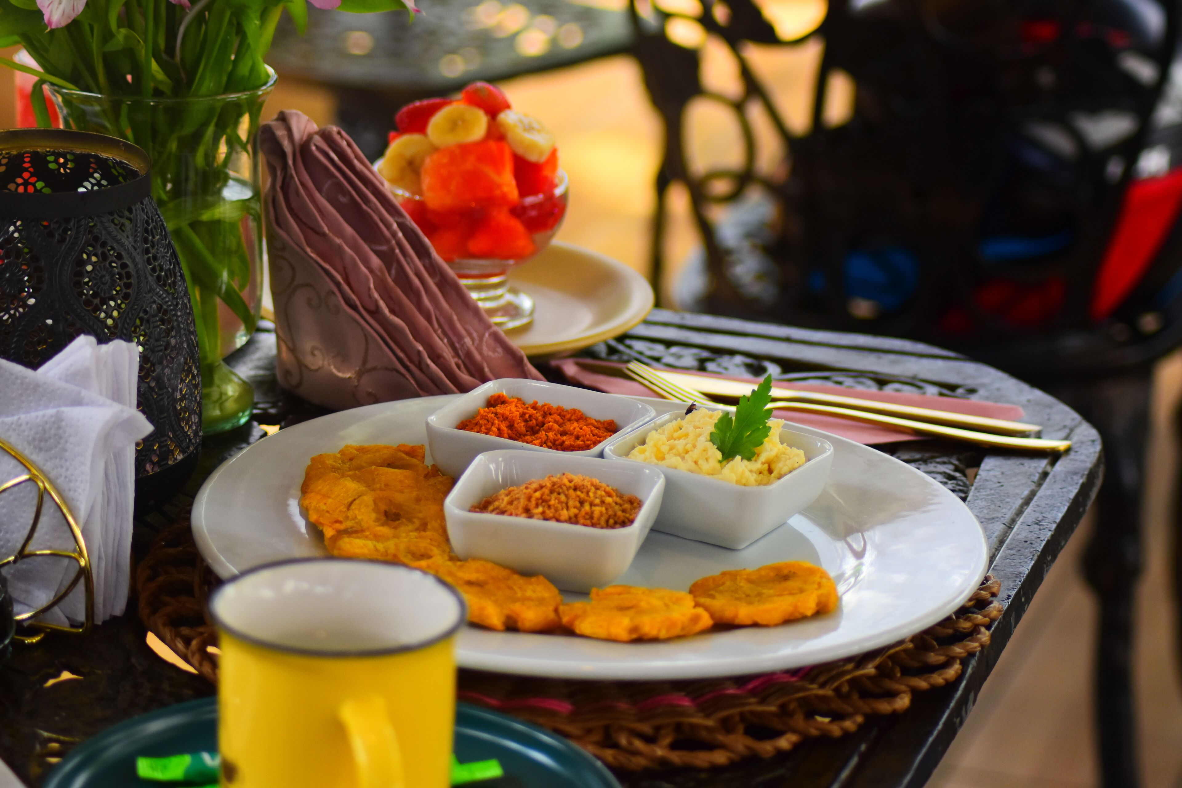 Une table avec une assiette de nourriture, comprenant des plats frits et un saladier de fruits, ainsi qu'une barre chocolatée.