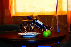 A table with a plate, two glasses, a bottle, and a green apple.