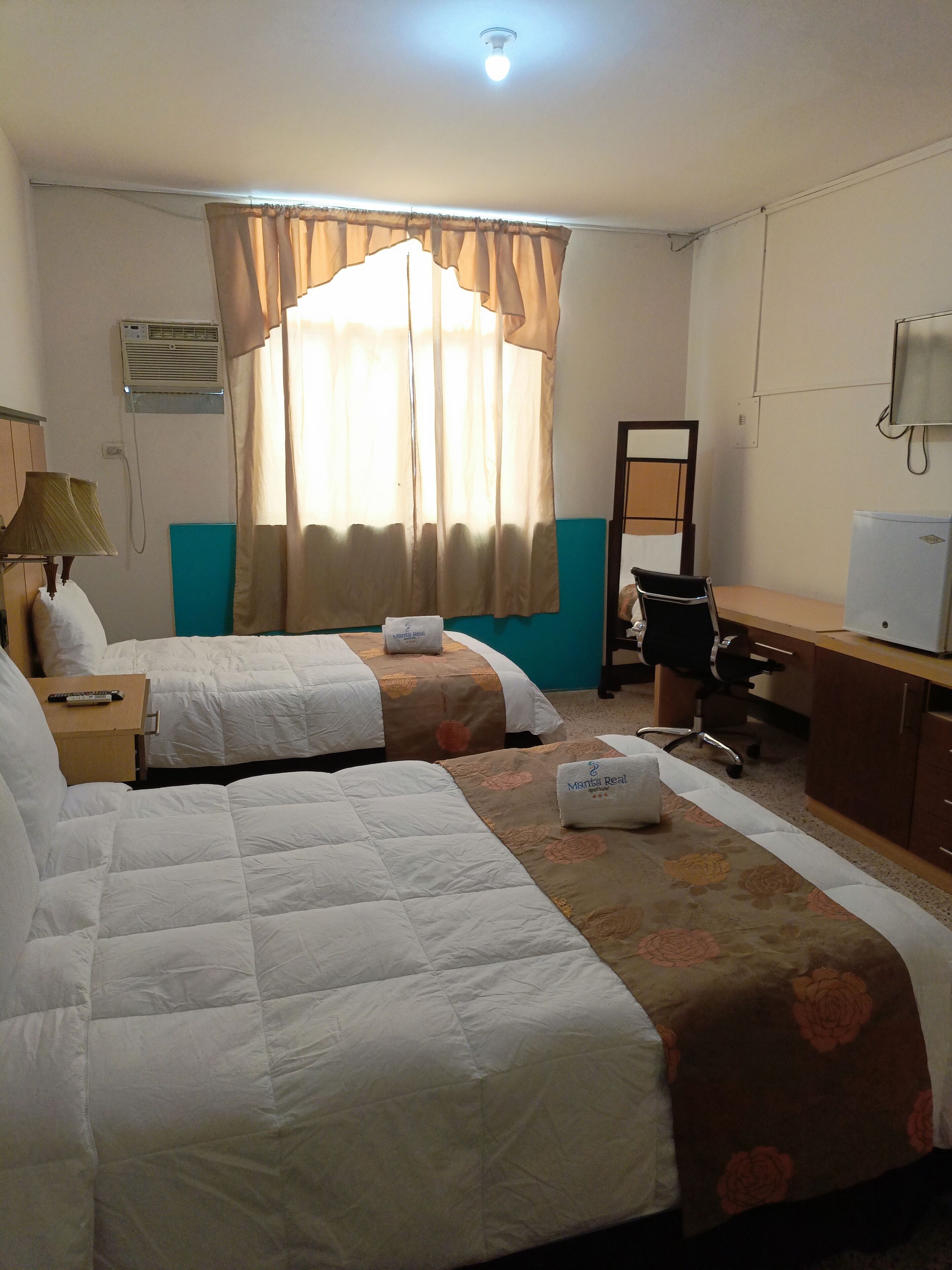 A hotel room with two beds, a desk, a chair, a mirror, and a television.