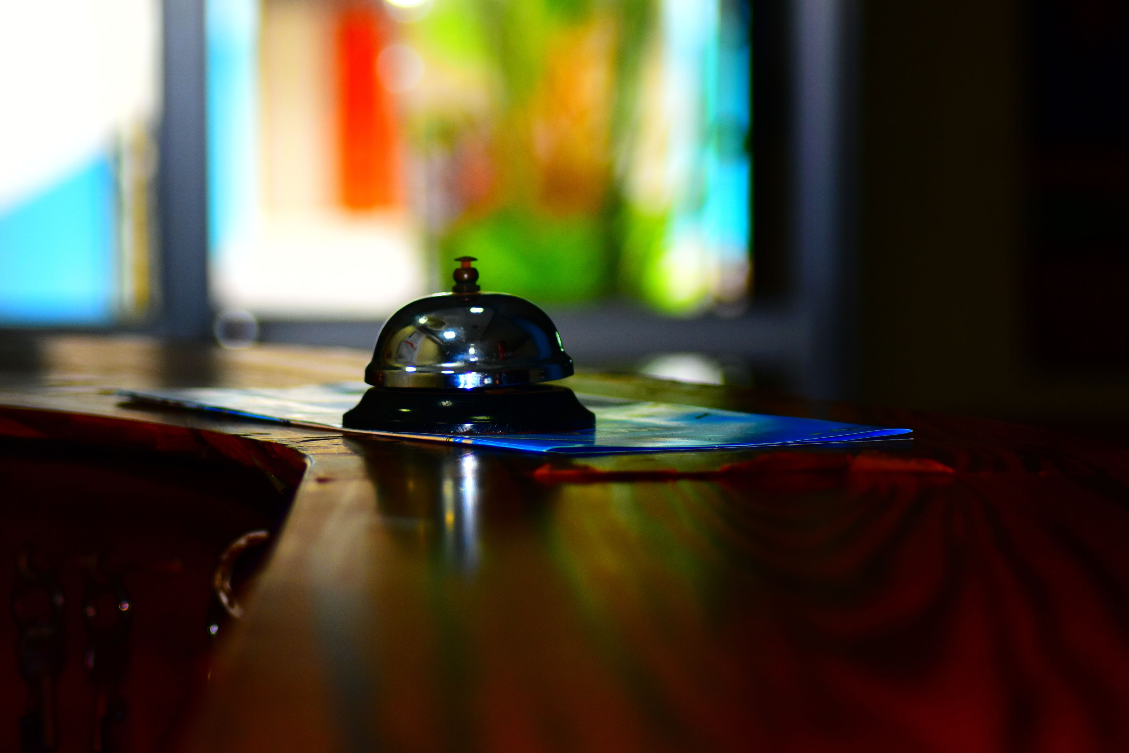 A bell on a table with a colorful stained glass window in the background.
