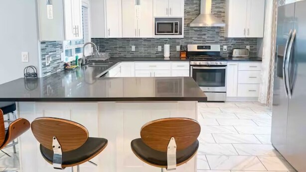 A modern kitchen with white cabinets, a central island, and a stainless steel refrigerator.