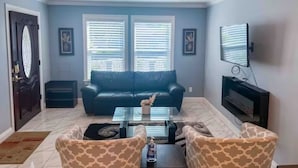 A living room with a blue sofa, patterned armchairs, a coffee table, and a flat-screen TV mounted on the wall.