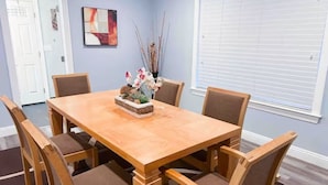 A dining room with a wooden table and six chairs, a vase with flowers, and a painting on the wall.