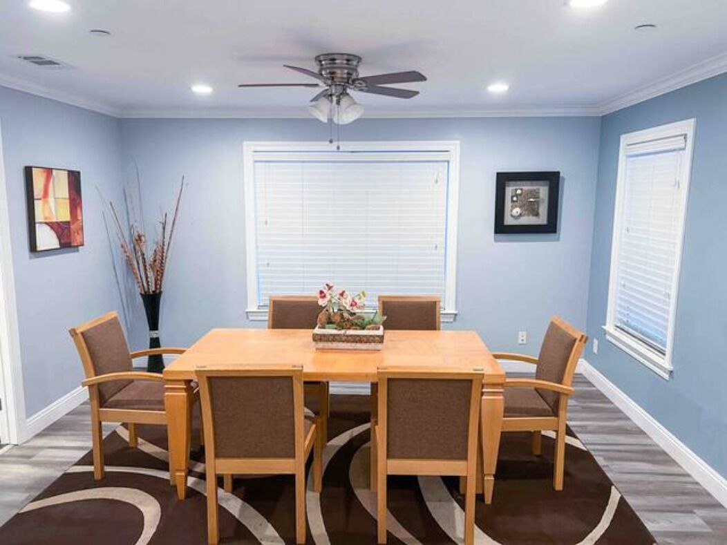 A dining room with a wooden table and chairs, a ceiling fan, and a window with blinds.