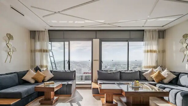 A modern living room with two sofas, a coffee table, and a large window with a city view. - Appartement Haut Standing Tanger (Tangier)