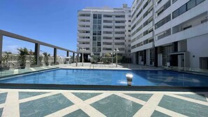 A swimming pool with a geometric tile pattern, surrounded by a building with multiple floors and balconies. - Appartement Haut Standing Tanger (Tangier)