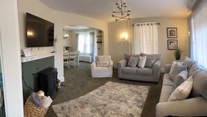 Una sala de estar con chimenea, sofás, televisión y un comedor al fondo.