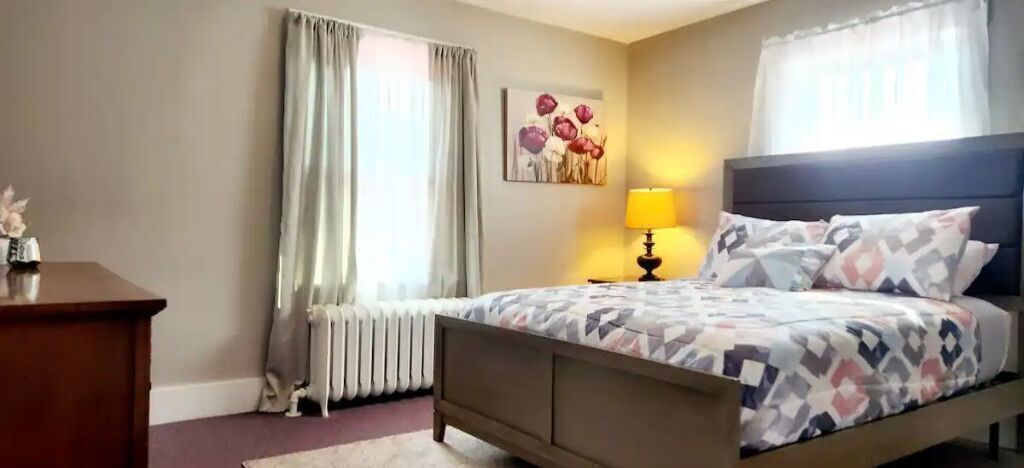 Ein Schlafzimmer mit einem Bett, einem Nachttisch, einer Lampe, einem Heizkörper und einem Bild an der Wand.
