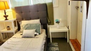 Un dormitorio ordenado con cama, mesitas de noche, lámpara y una pequeña planta.
