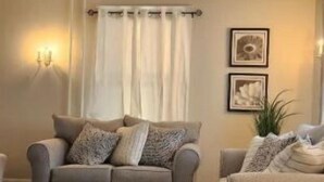 Una sala de estar con dos sofás, un tapete estampado, una araña y cuadros enmarcados en la pared.