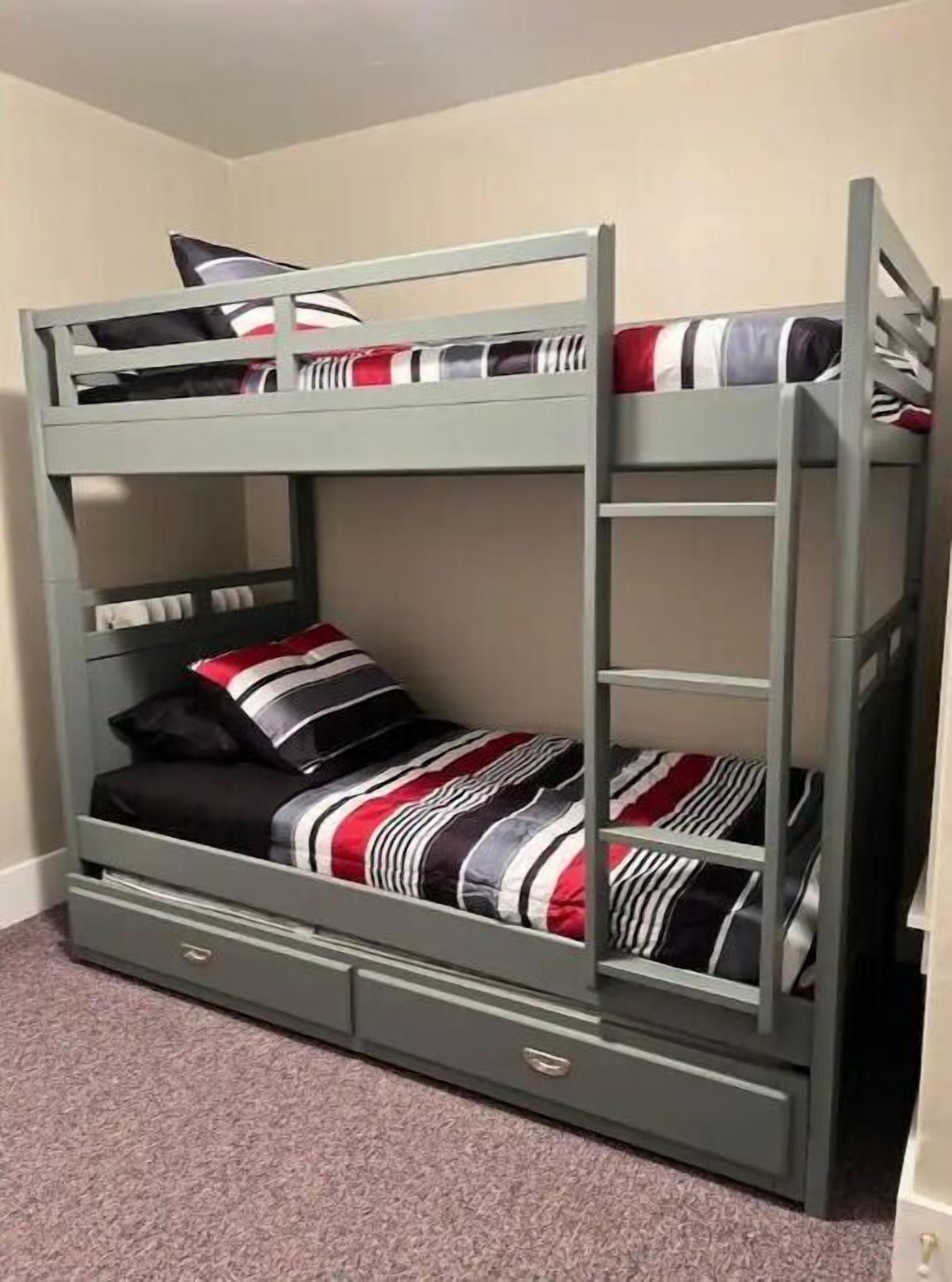 Ein Etagenbett mit einer Schublade unter dem unteren Bett, einer gestreiften Decke und einem Kopfkissen.