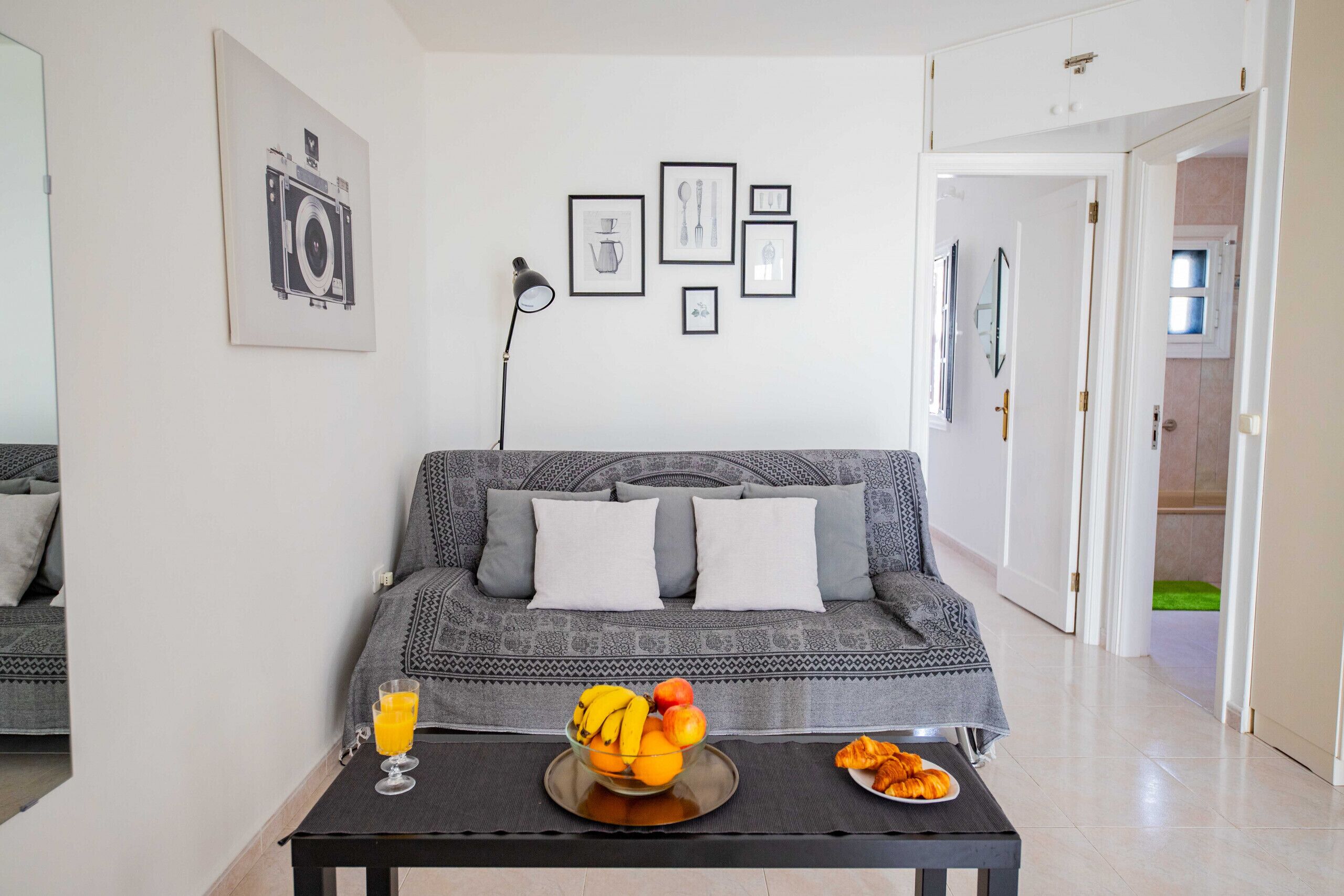 A living room with a sofa, a coffee table with fruit and a glass of juice, and framed pictures on the wall.