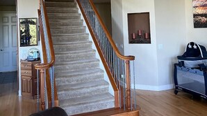 Un vaste espace de vie agrémenté d’un escalier en bois, d’un canapé en cuir noir et d’un parc pour bébé.