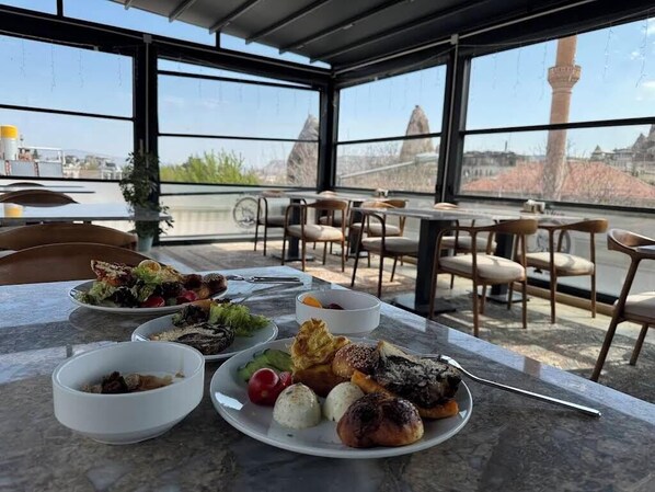Un espace repas avec des sièges en plein air, une table dressée avec différents plats, et une vue sur une tour en arrière-plan.