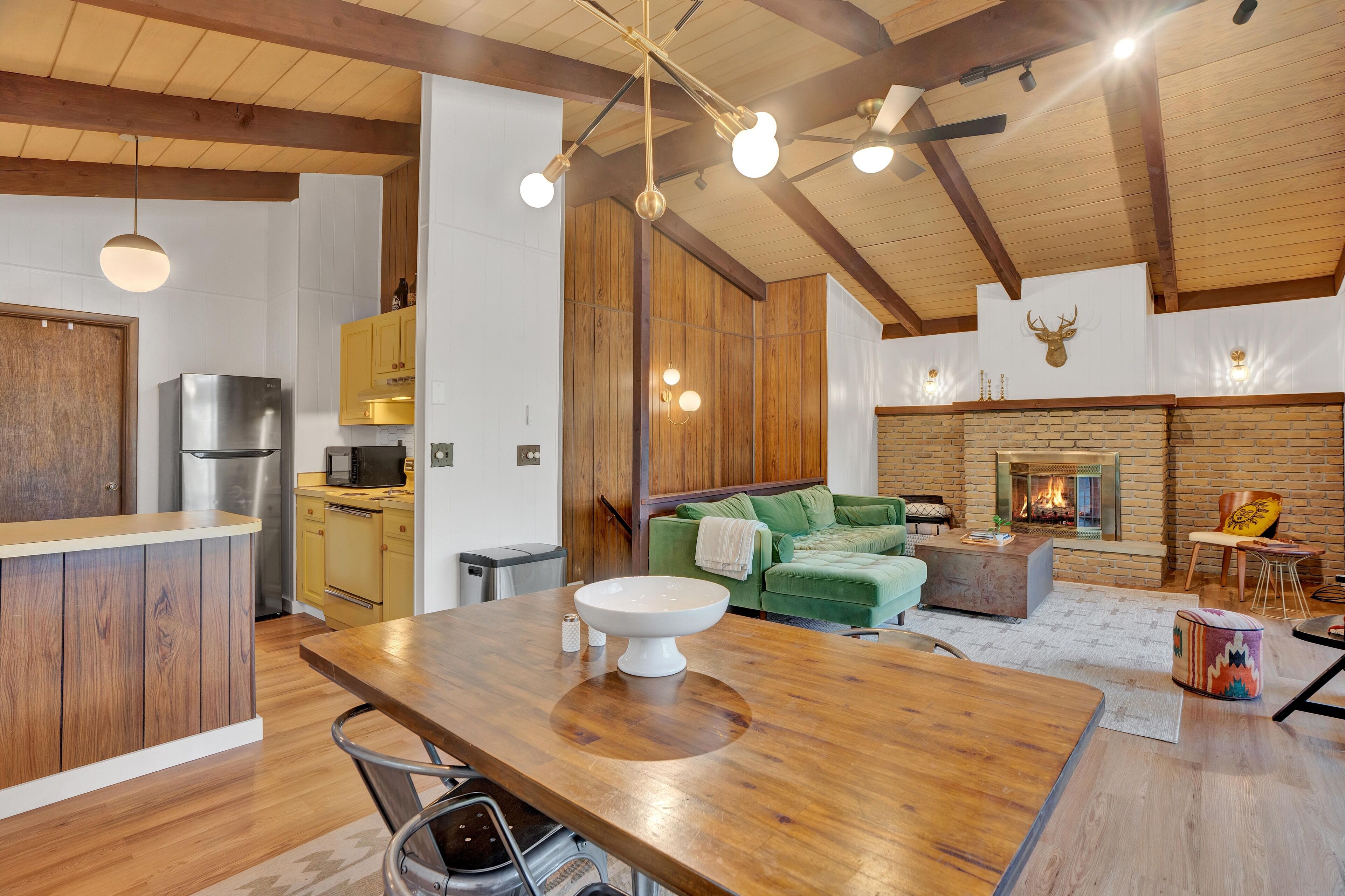 Una cocina moderna con armarios de madera, un refrigerador de acero inoxidable y una zona de comedor con una mesa de madera.