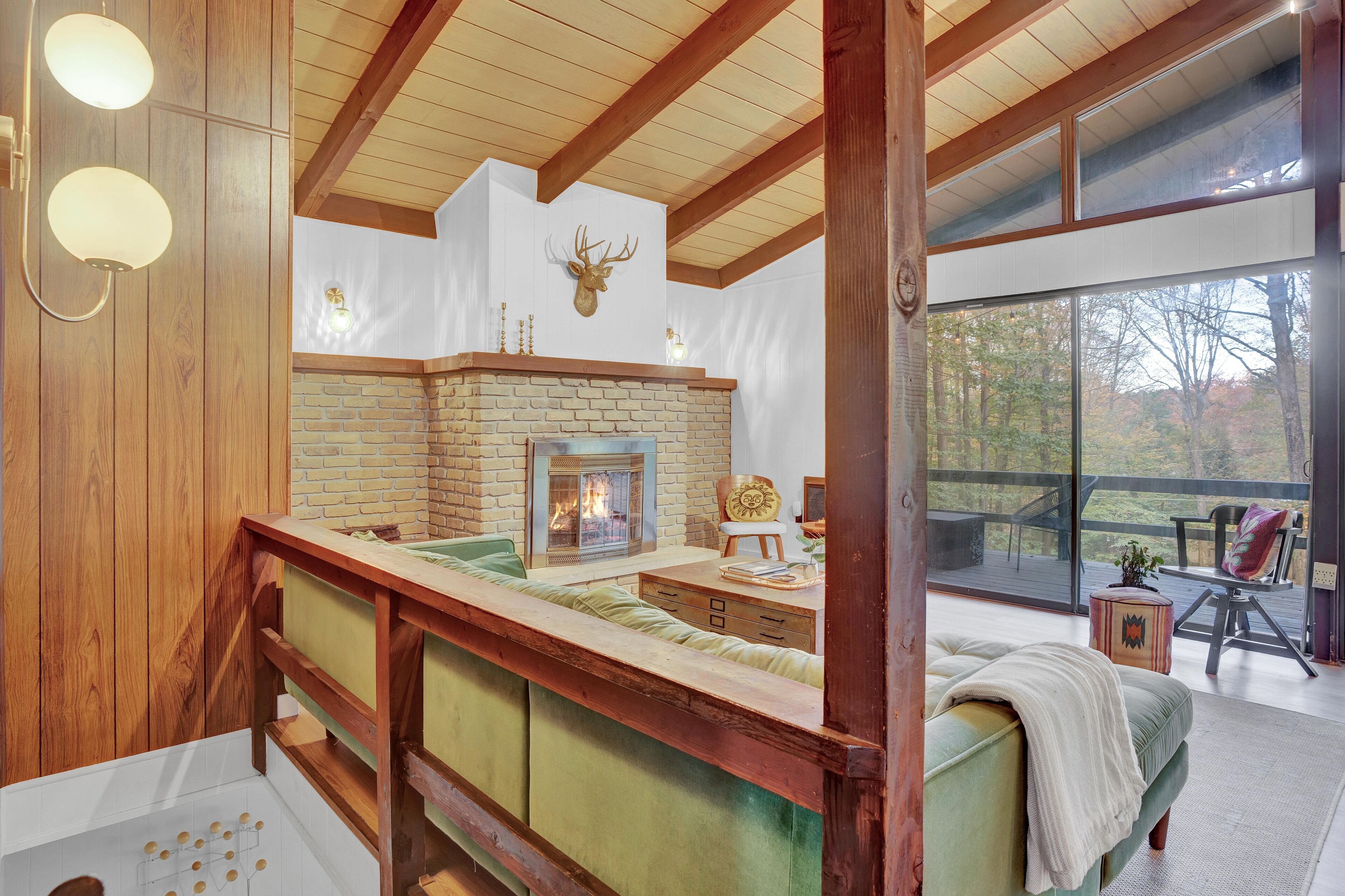 Una sala de estar acogedora con chimenea de ladrillo, vigas de madera y un ventanal con vistas a una terraza.