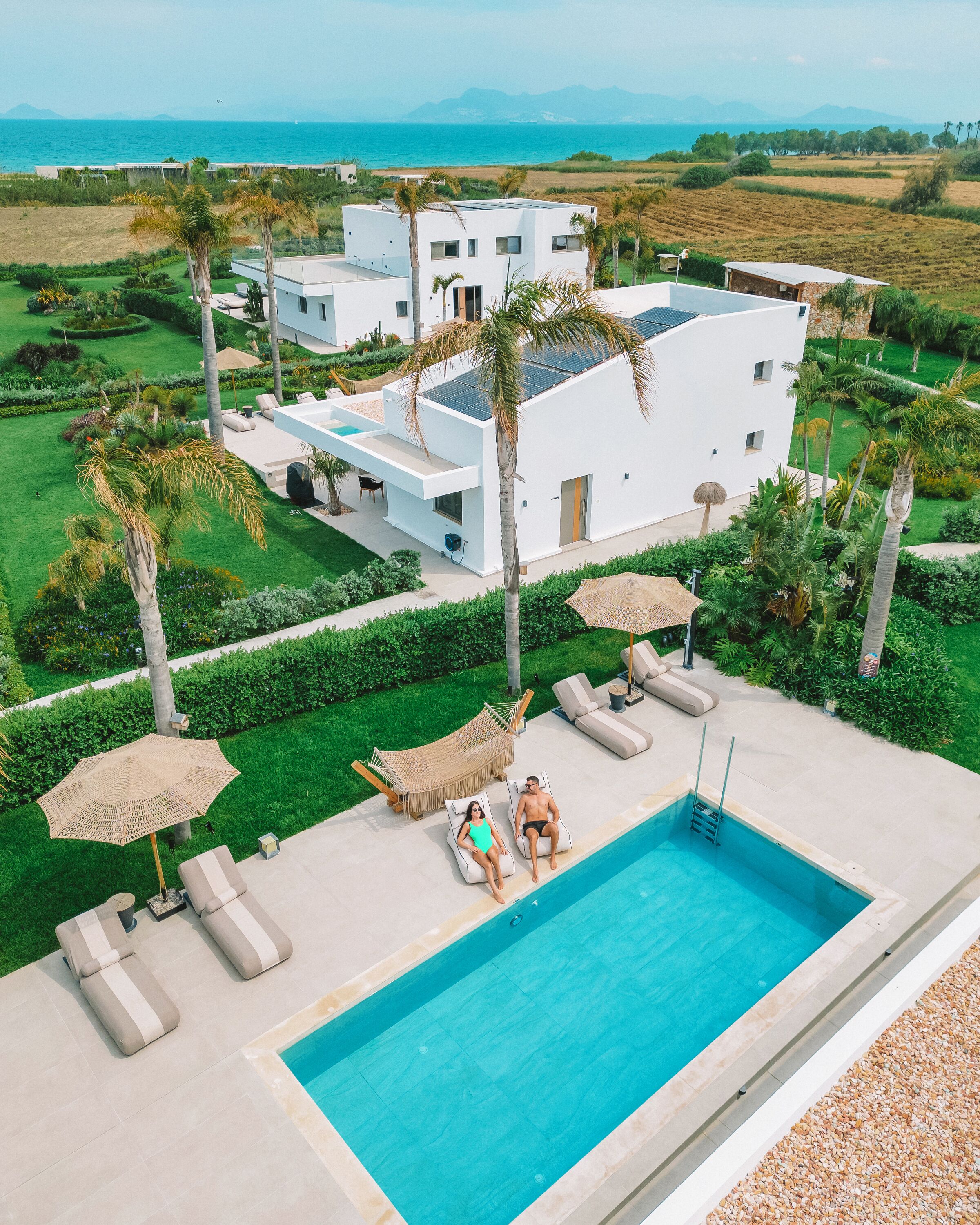 A modern villa with a swimming pool, surrounded by lush greenery and a view of the sea.