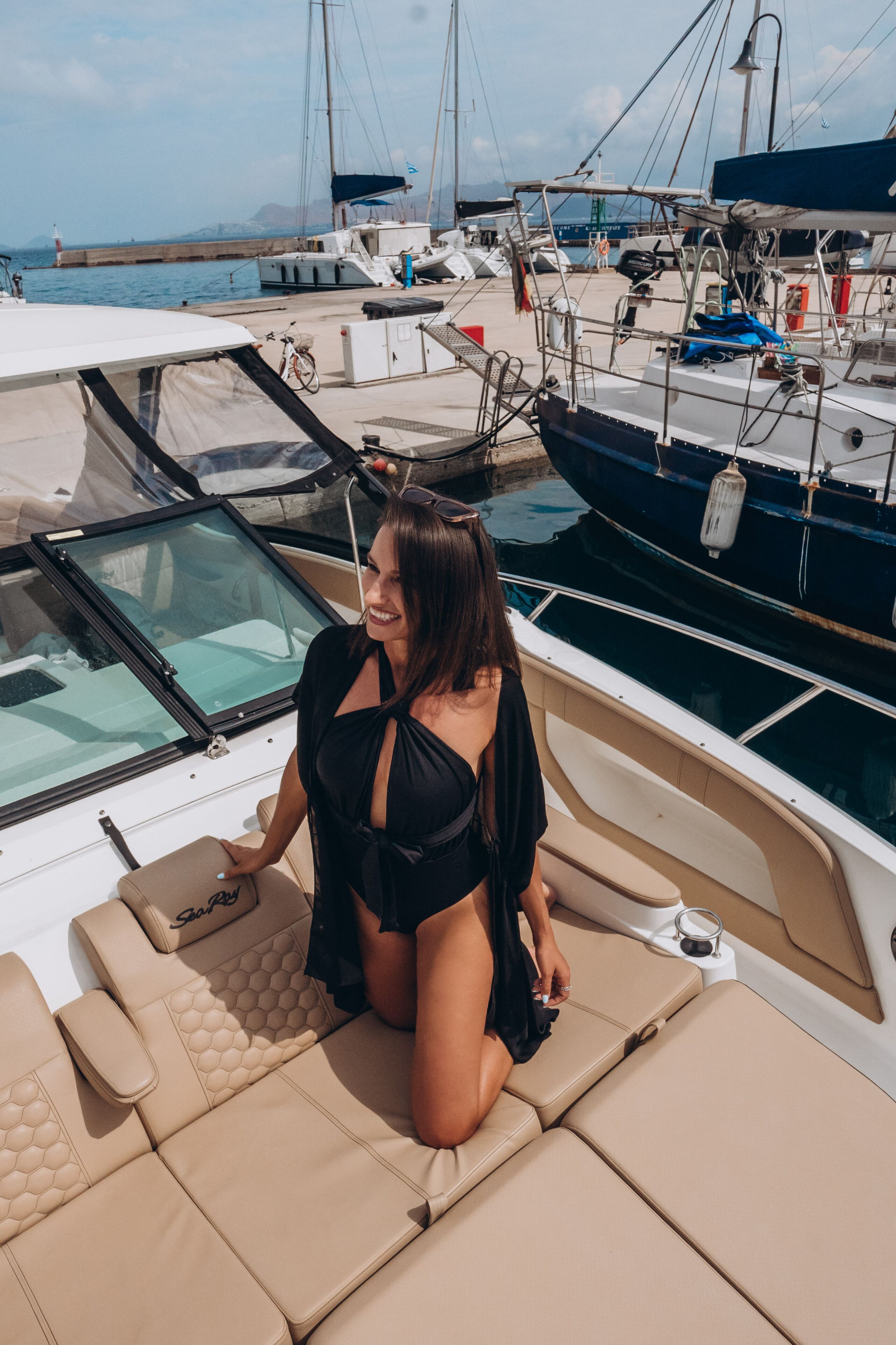A woman sitting on a boat deck with a view of other boats and a lighthouse in the background.
