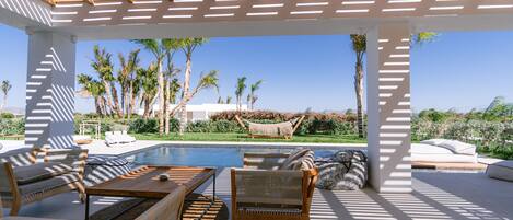A covered outdoor area with a pool, lounge chairs, and a hammock.