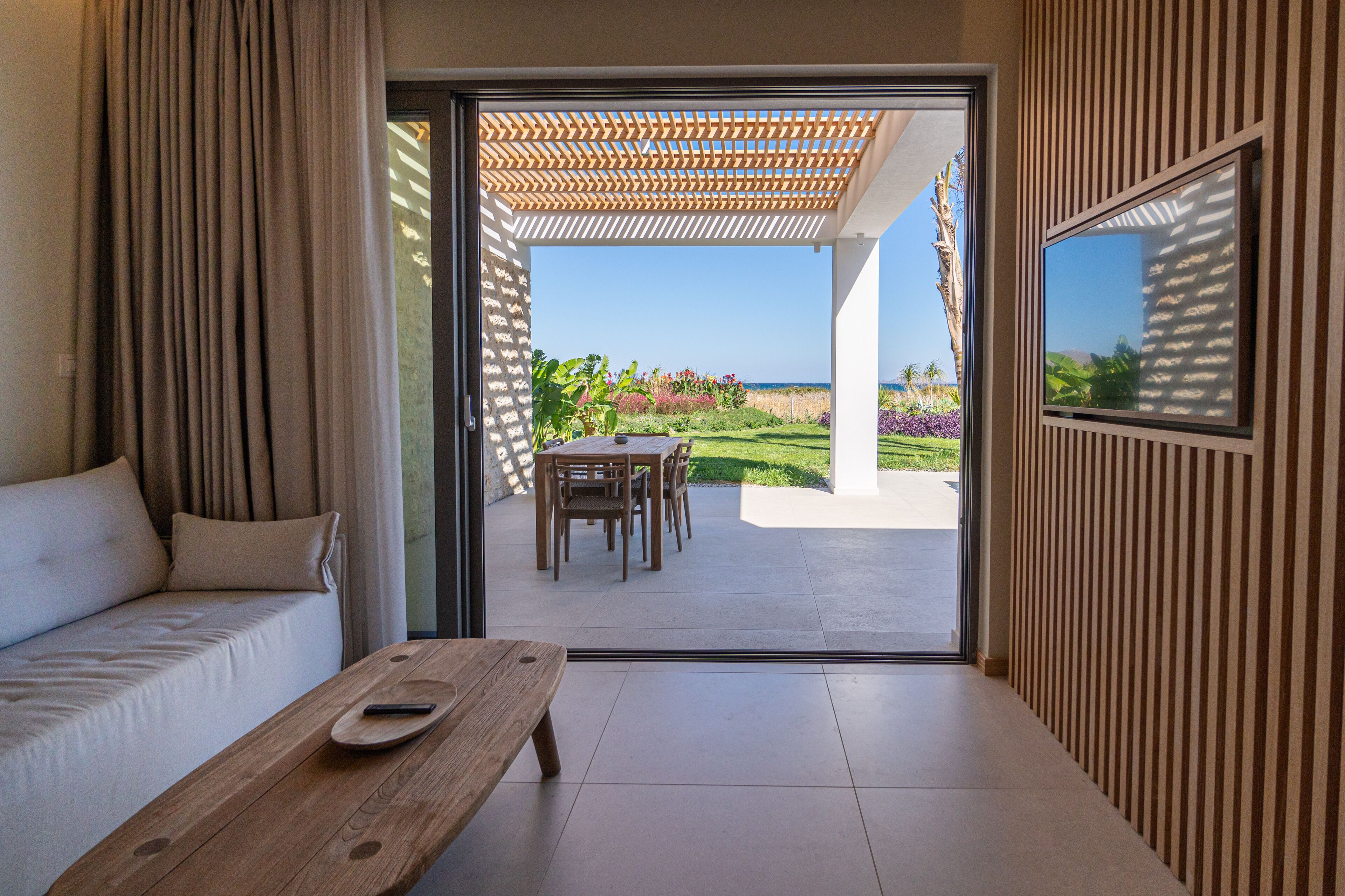 A modern room with a sofa, a wooden table, and a view of an outdoor patio with a table and chairs.