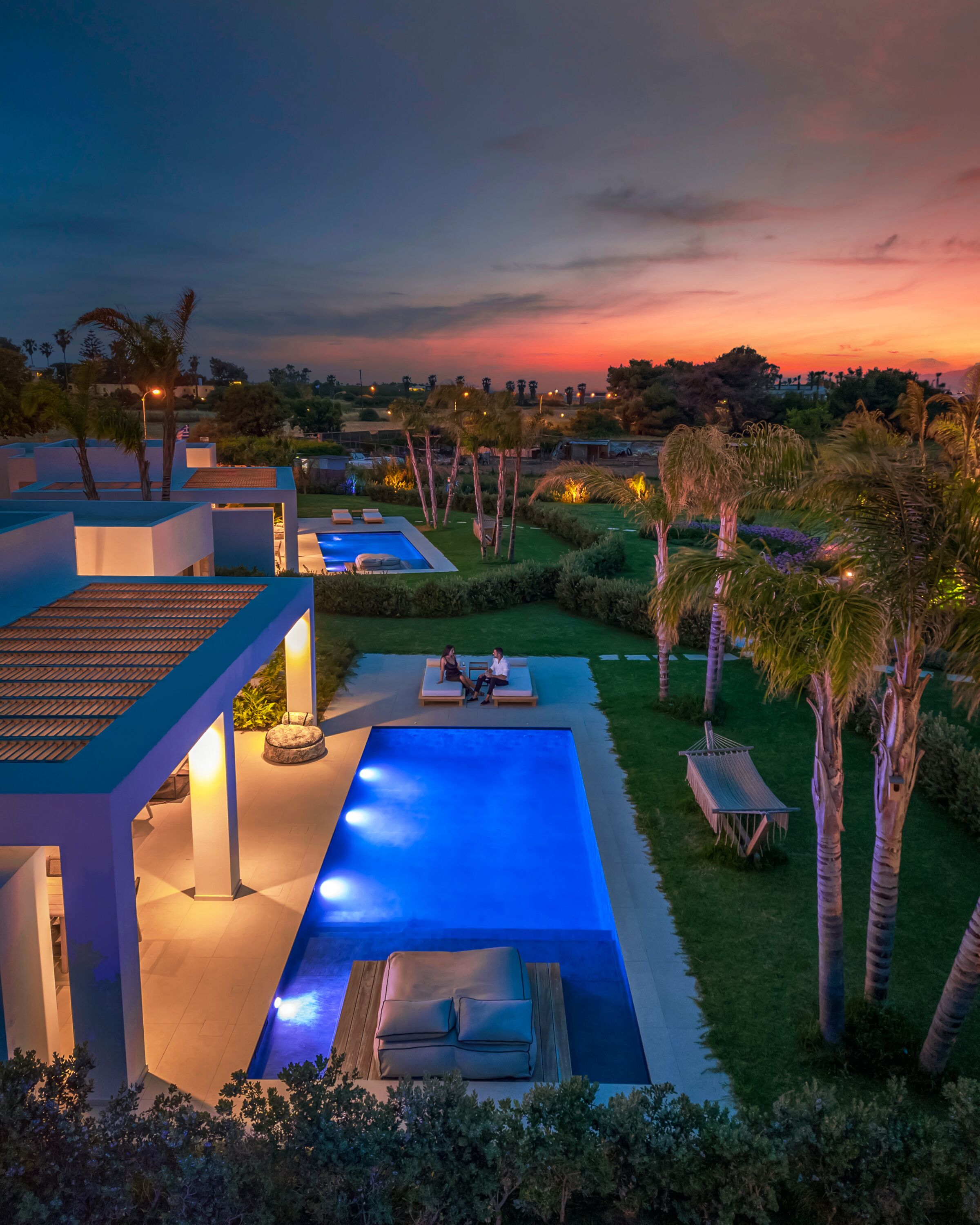 A modern outdoor pool area with a rectangular pool, lounge chairs, and a seating area with two people.