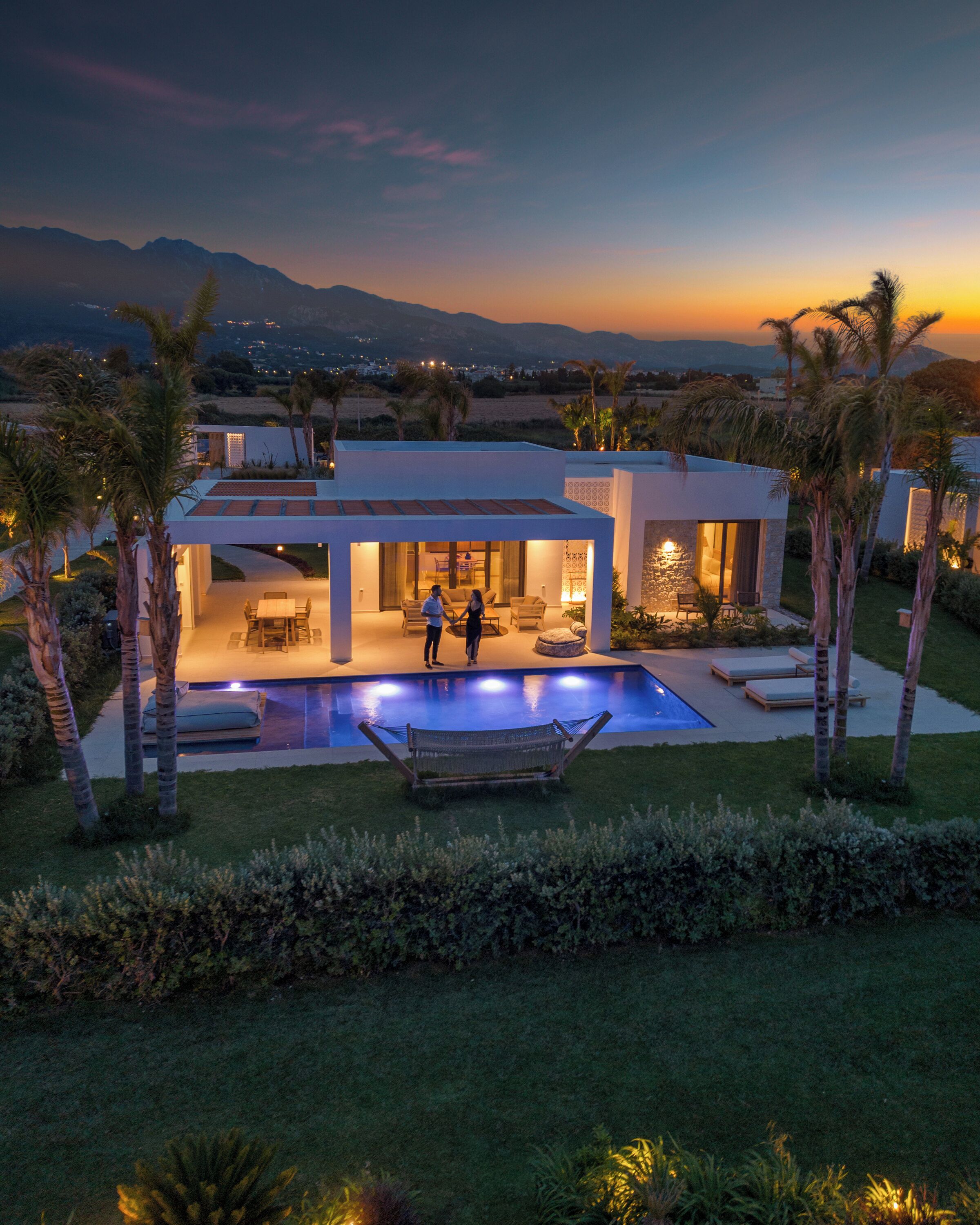 Una casa moderna con piscina, mobiliario exterior y palmeras.