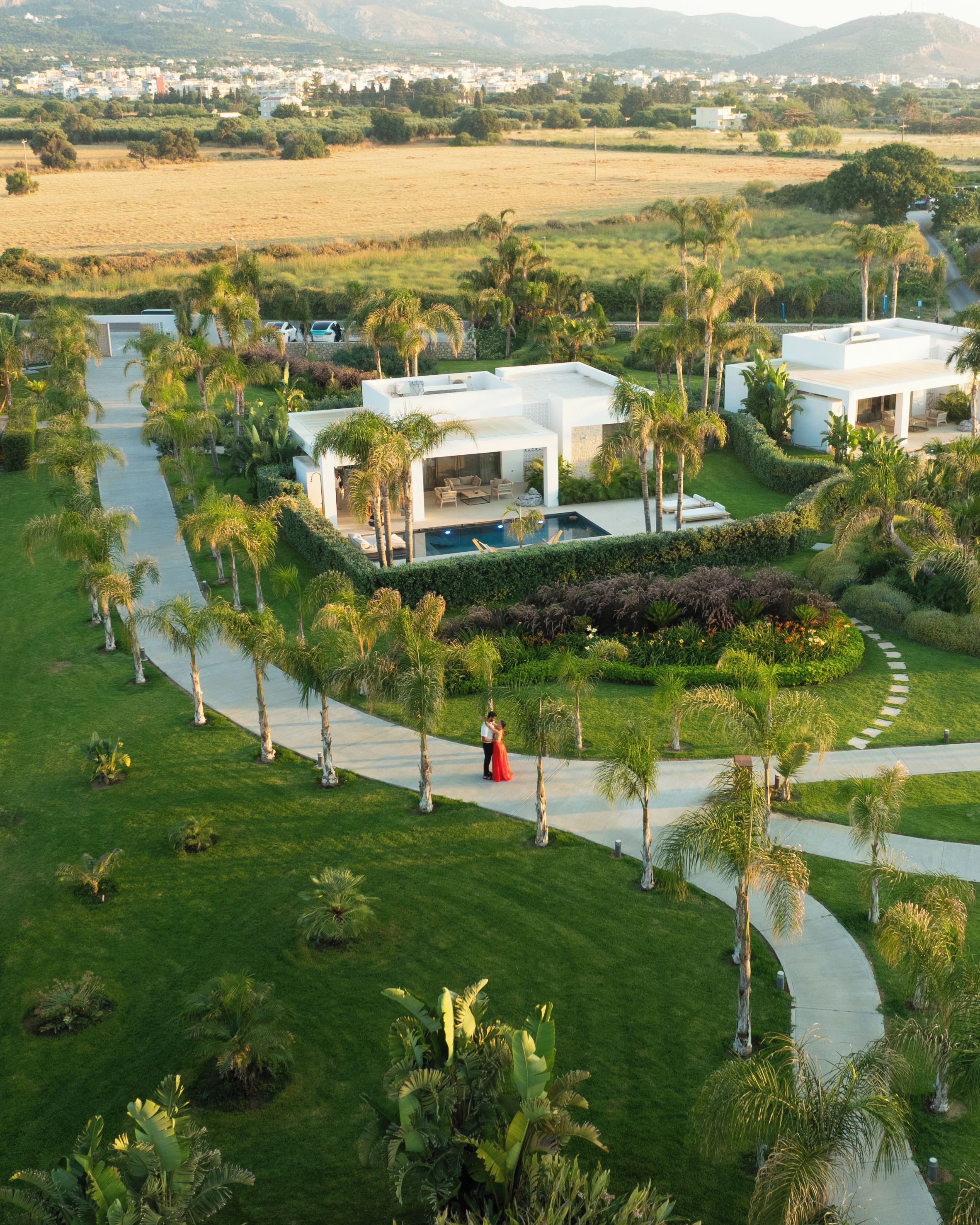 A modern resort with a pool, palm trees, and a well-maintained lawn.
