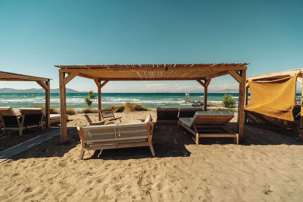 A beach with wooden structures, including a covered seating area and lounge chairs, overlooking the sea.