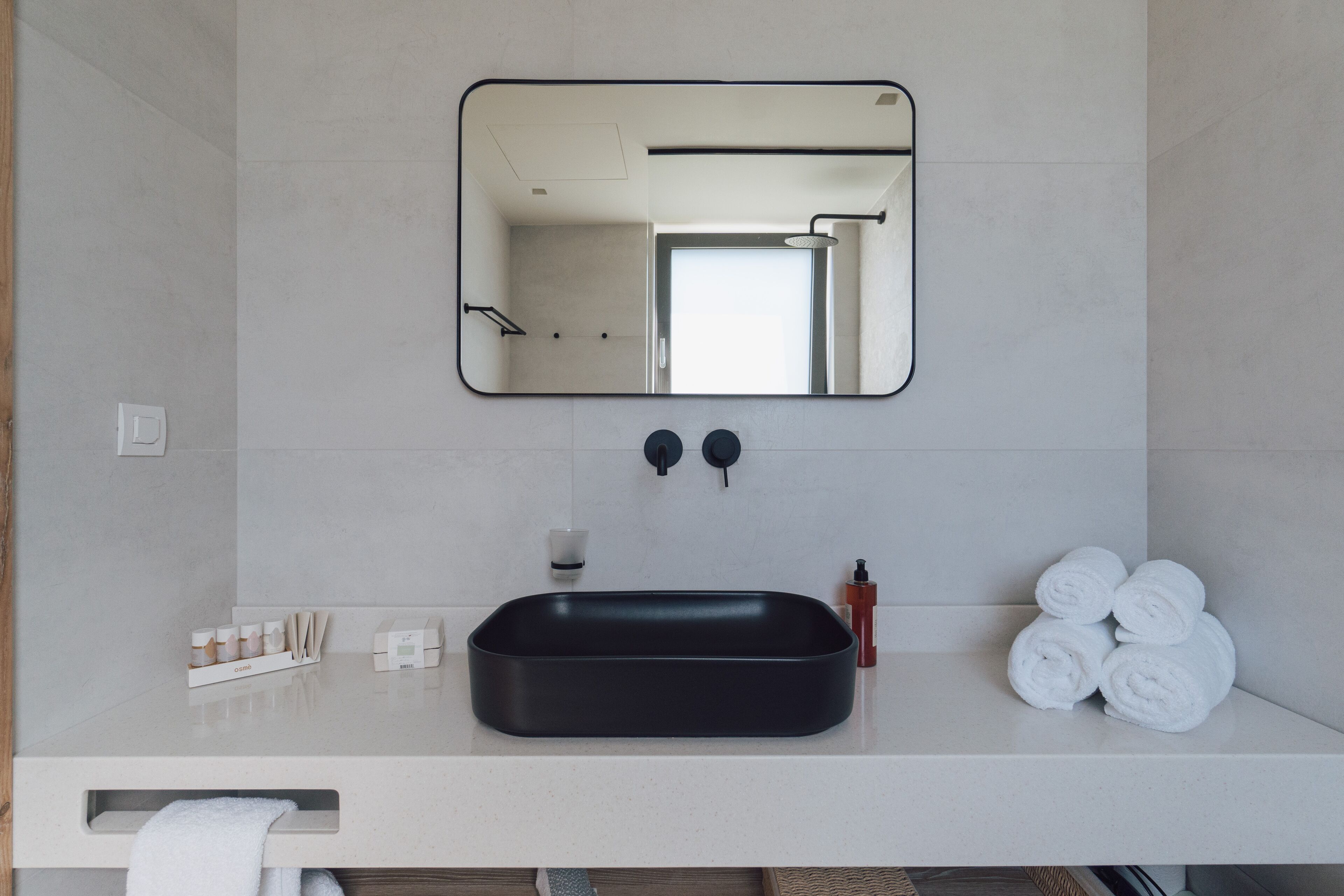 A modern bathroom with a black sink, a large mirror, and neatly rolled white towels.