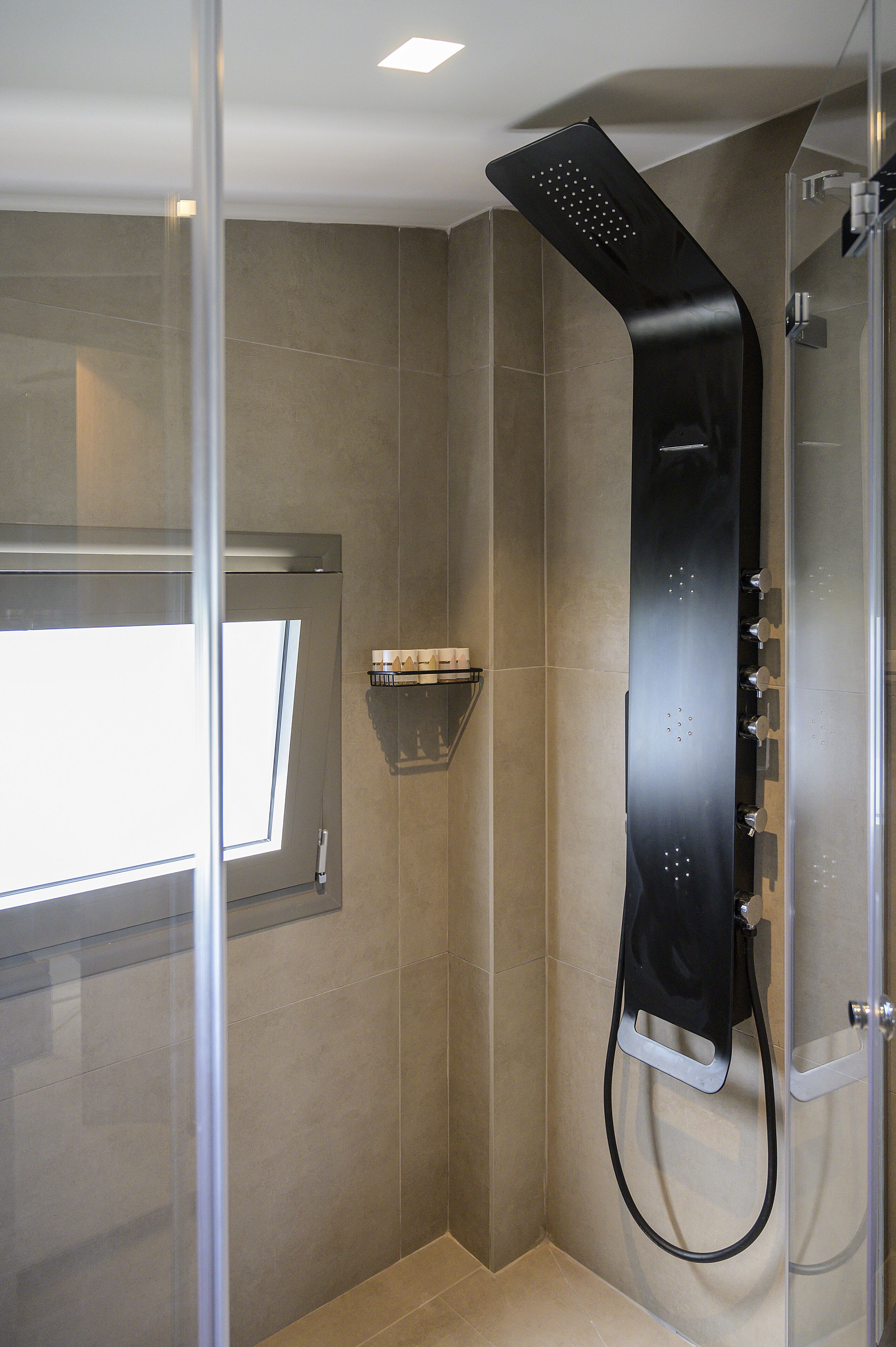 A modern shower with a curved design, a glass door, and a small shelf with toiletries.