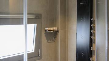 A modern shower with a curved design, a glass door, and a small shelf with toiletries.