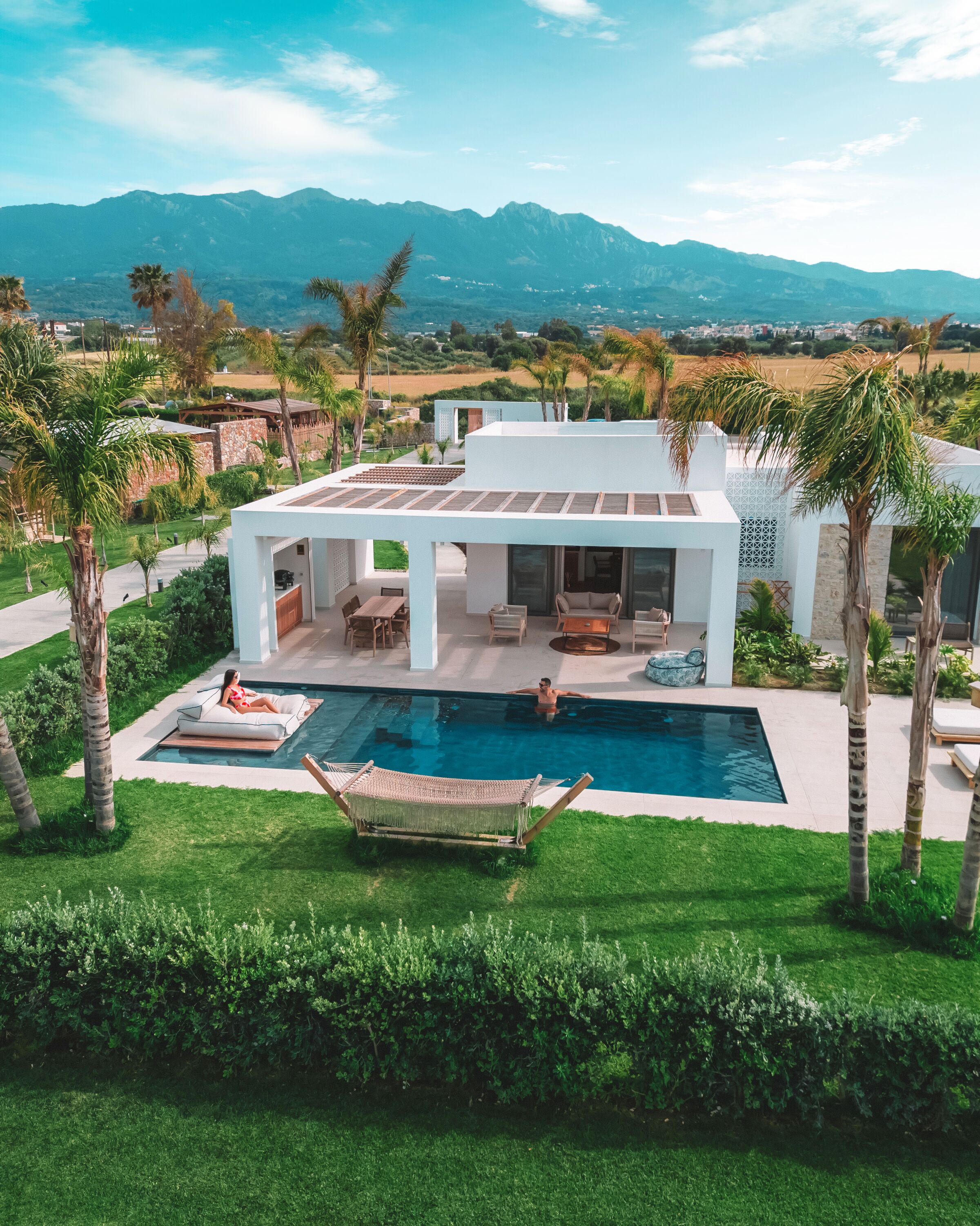 A modern house with a swimming pool, patio furniture, and a hammock.