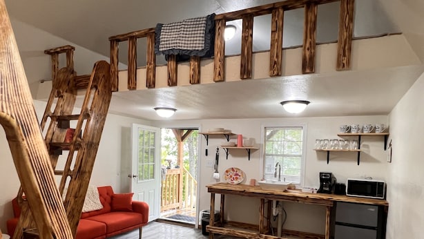 Cocina pequeña con escalera de madera, sofá rojo y zona de comedor.
