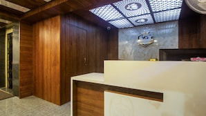 A hotel reception area with a wooden panel wall, a marble countertop, and a ceiling with a geometric pattern. - Itsy Hotels Yogeshwara Grand (Hyderabad)